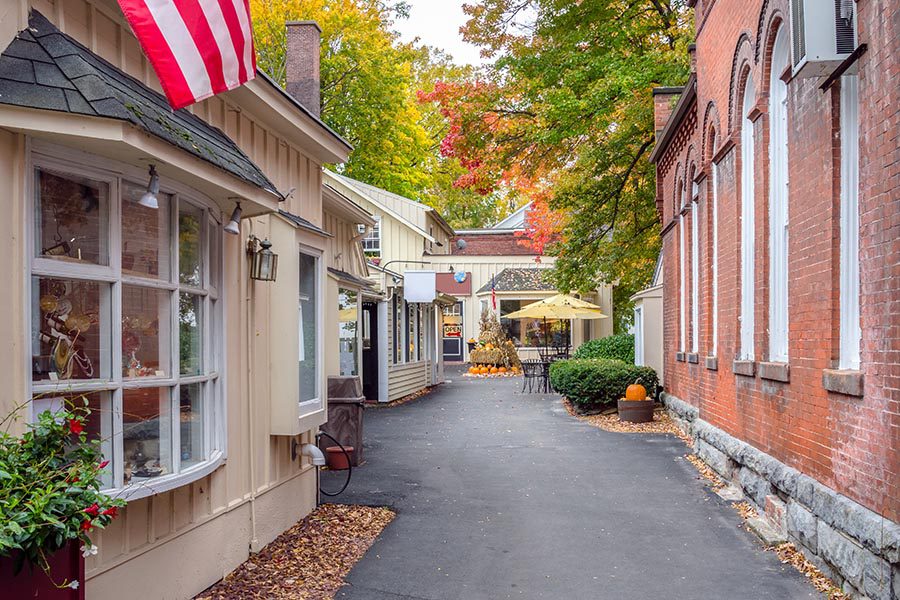 Homepage - Shops in Virginia With Glass Display Windows and Brick Facades, Leaves and Pumpkins Lining the Road